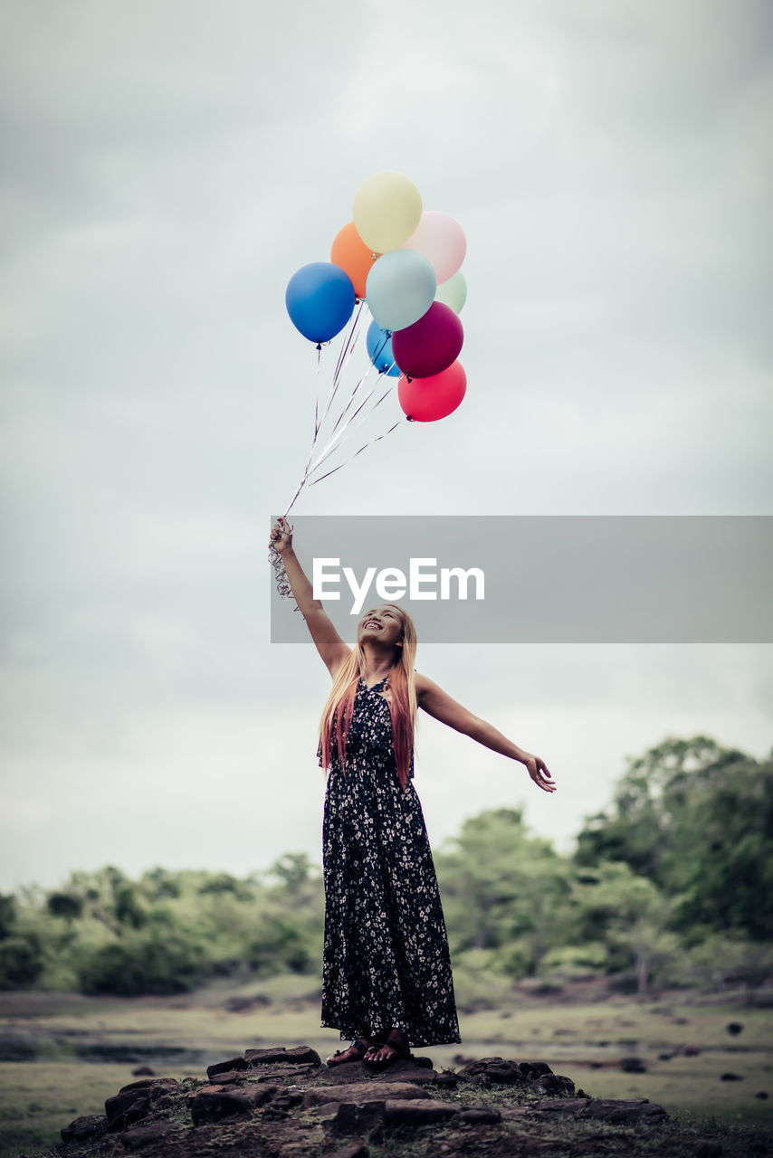 Full length of woman holding balloons while standing against sky