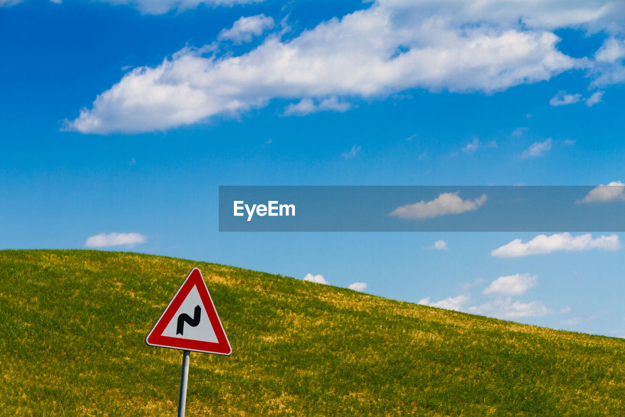 ROAD SIGN ON FIELD AGAINST BLUE SKY