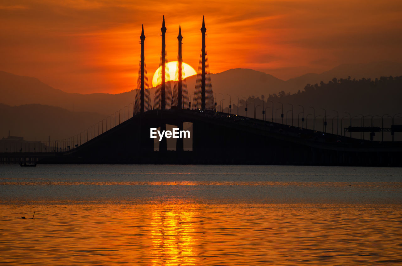 SILHOUETTE BRIDGE OVER BAY AGAINST SKY DURING SUNSET