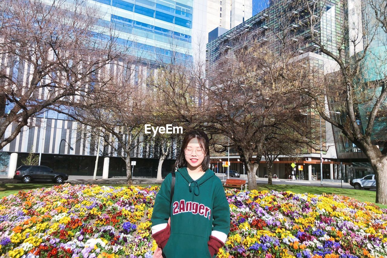 PORTRAIT OF SMILING WOMAN STANDING BY PLANTS