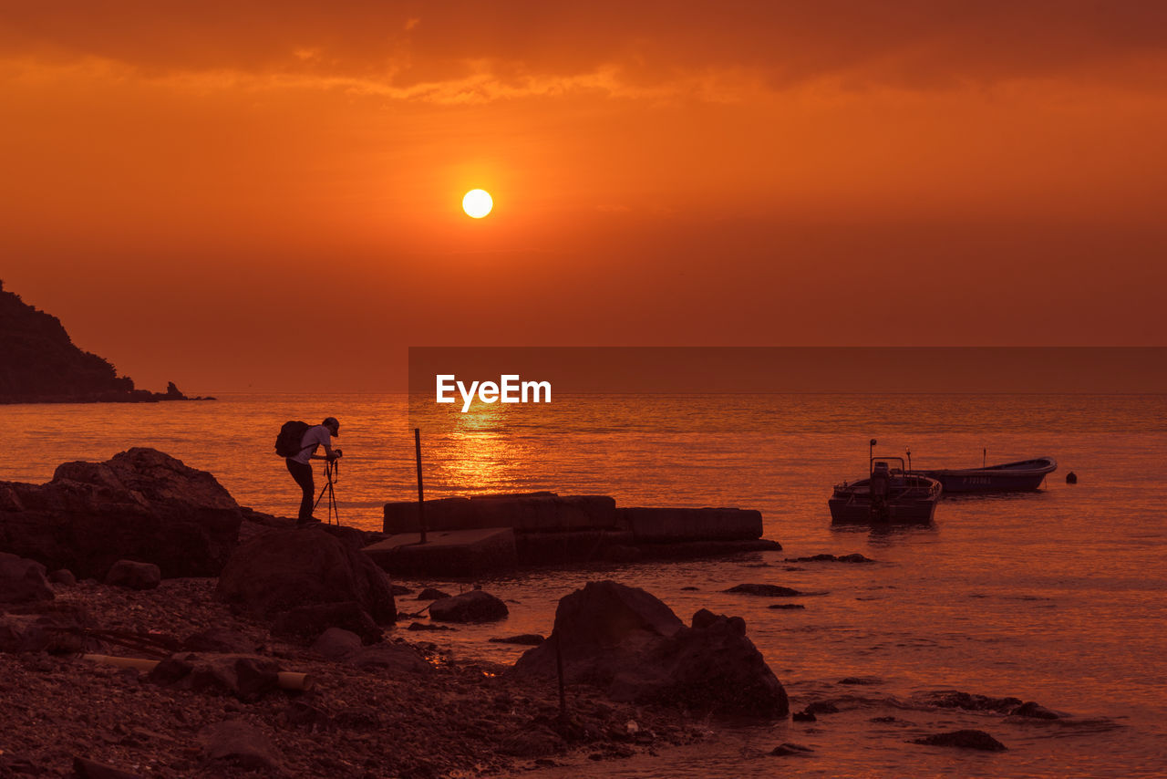 Man photographing at beach against sky during sunset