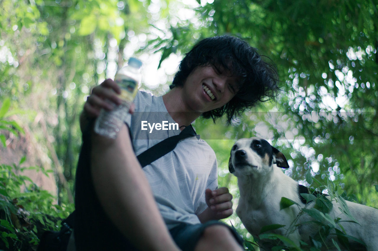 Low angle view of young man sitting with dog at forest