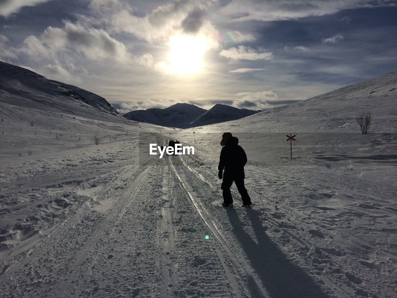 Rear view of man walking on snow covered field against cloudy sky