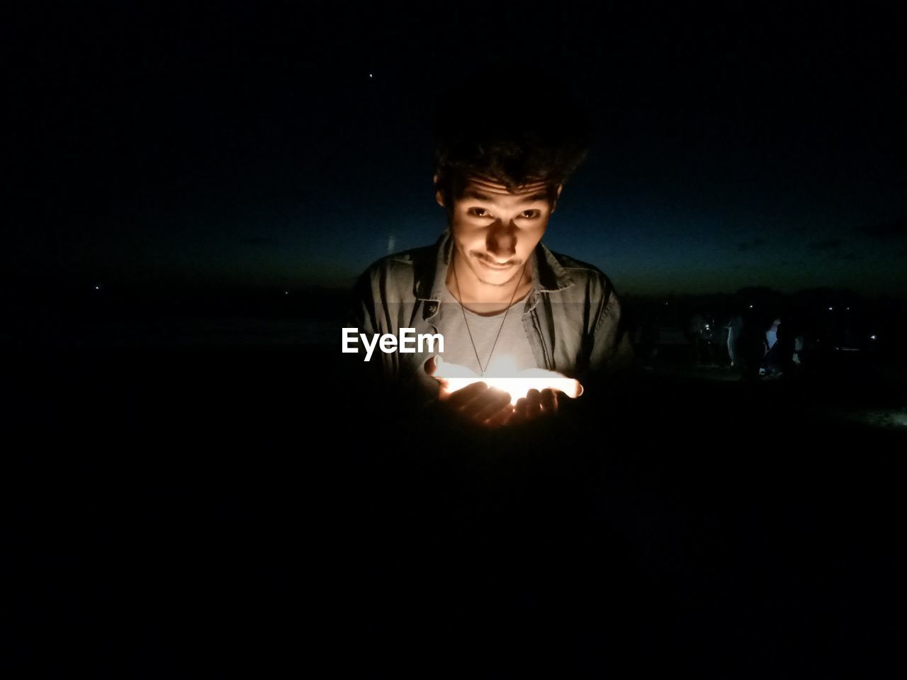Portrait of man holding illuminated light against sky at night