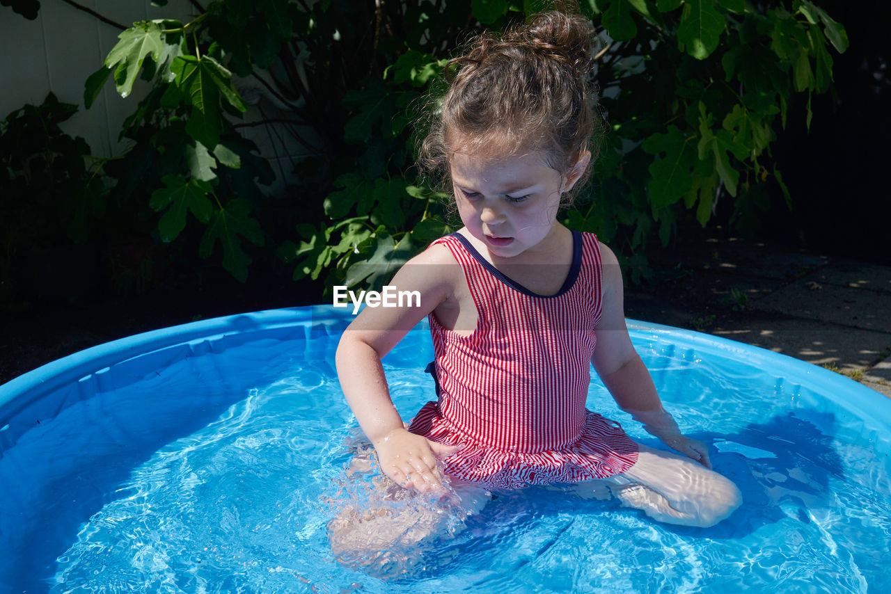 Cute toddler playing in the water basin in the backyard