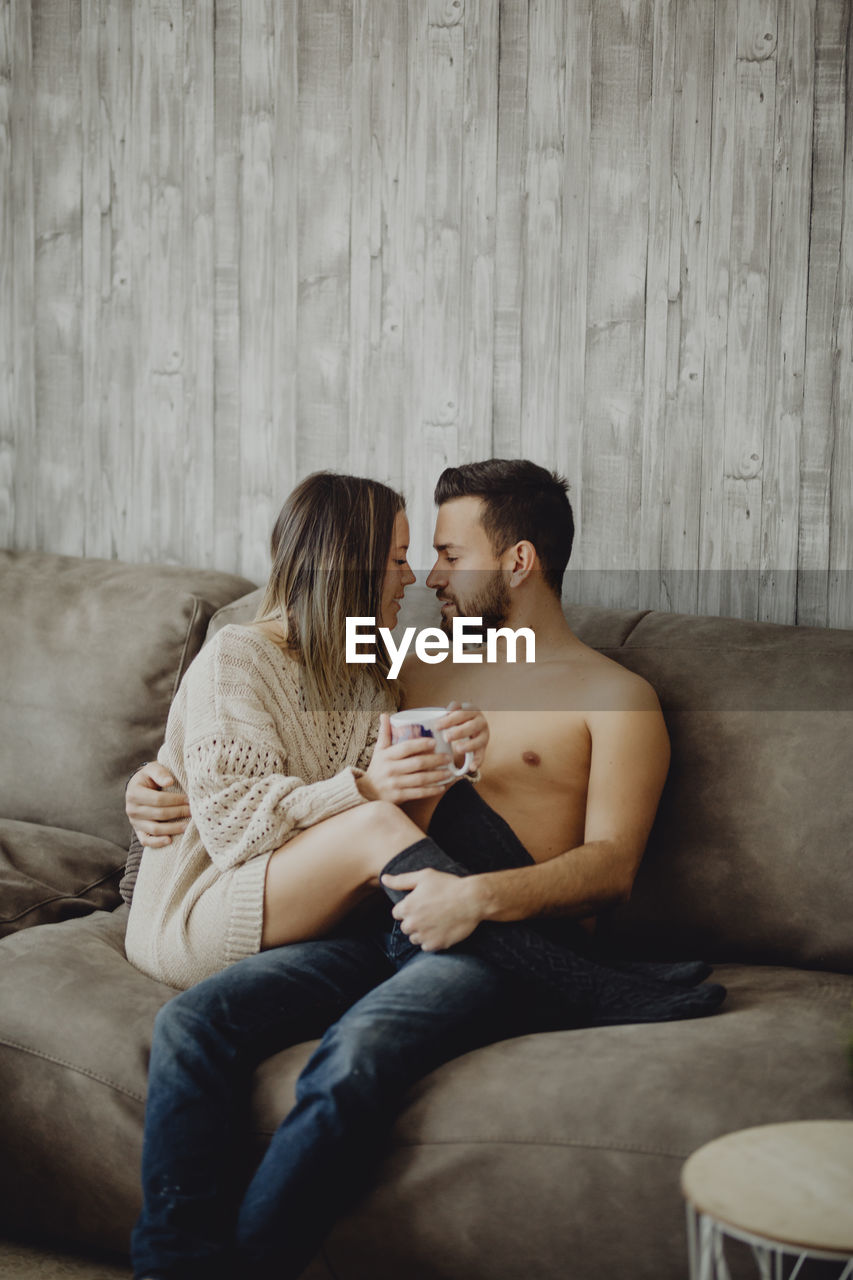 Happy man and woman with mug of hot beverage smiling and looking at each other while spending time at home in morning