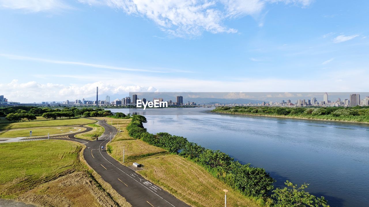 architecture, city, built structure, sky, water, landscape, river, building exterior, building, horizon, nature, cloud, urban skyline, environment, cityscape, travel destinations, waterway, travel, transportation, aerial photography, road, office building exterior, skyscraper, coast, no people, reservoir, reflection, scenics - nature, outdoors, tourism, street, plant, land, business finance and industry, skyline, day, body of water, residential district, high angle view, blue, shore, levee, city life, bridge, beauty in nature, tree, business, office, grass, construction industry, sunlight, highway, industry