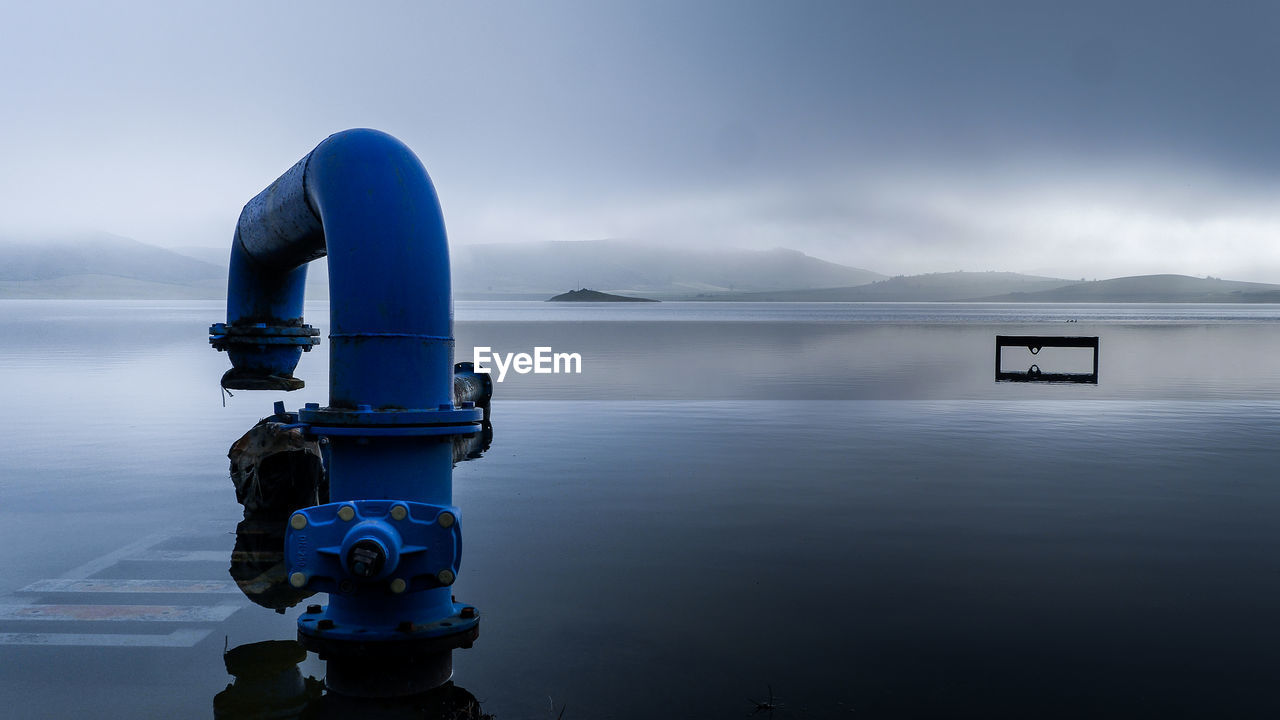 Pipe at lake against cloudy sky