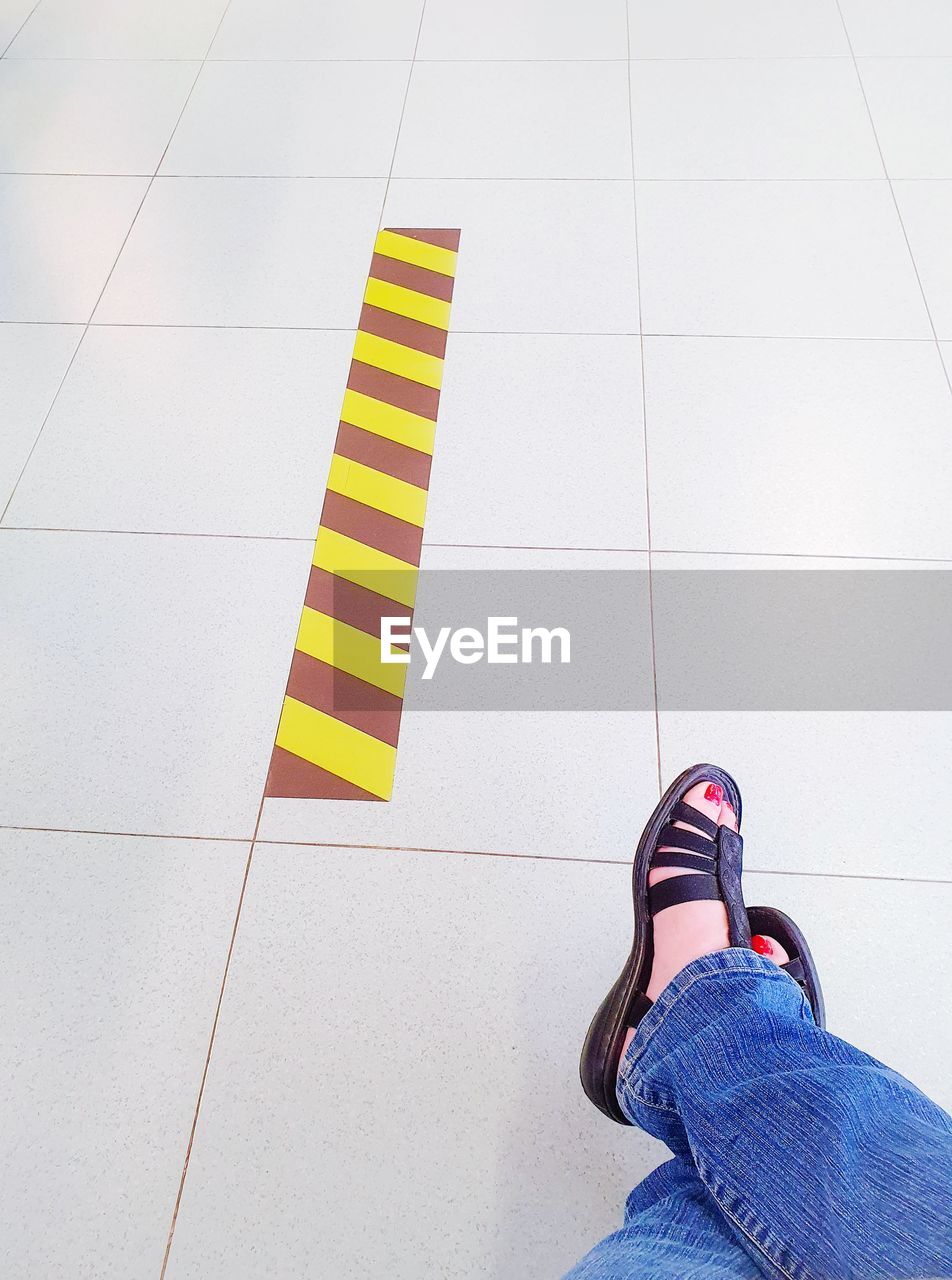 LOW SECTION OF WOMAN STANDING AGAINST TILED FLOOR