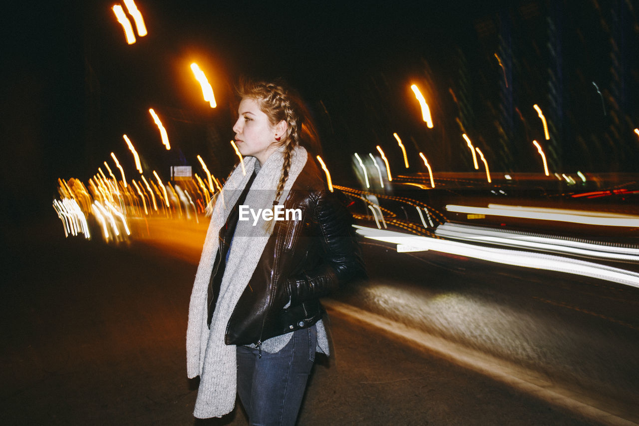 Young woman standing against light trails on road at night