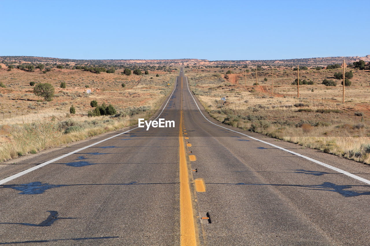 Empty long road amidst landscape against clear sky