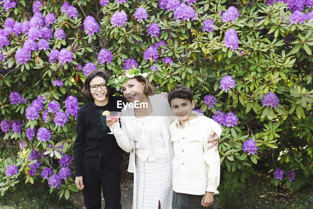 Portrait of smiling senior woman with grandsons against flowering plants