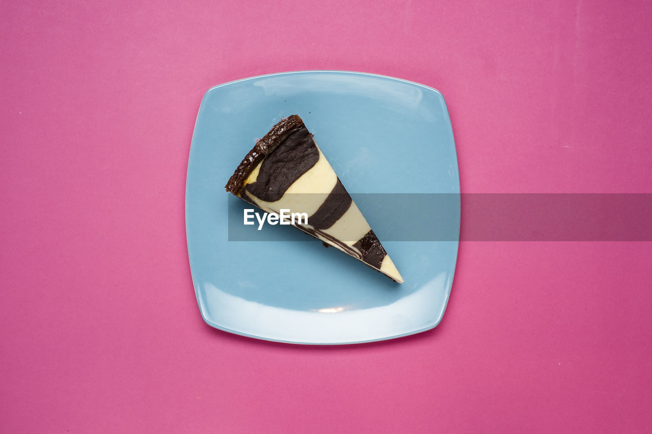Directly above shot of slice of cake in plate against pink background