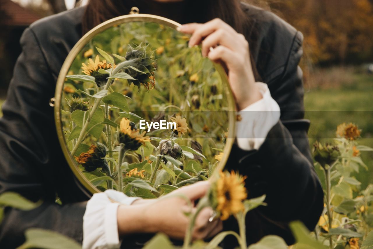 MIDSECTION OF WOMAN HOLDING FLOWERING PLANTS AT HOME