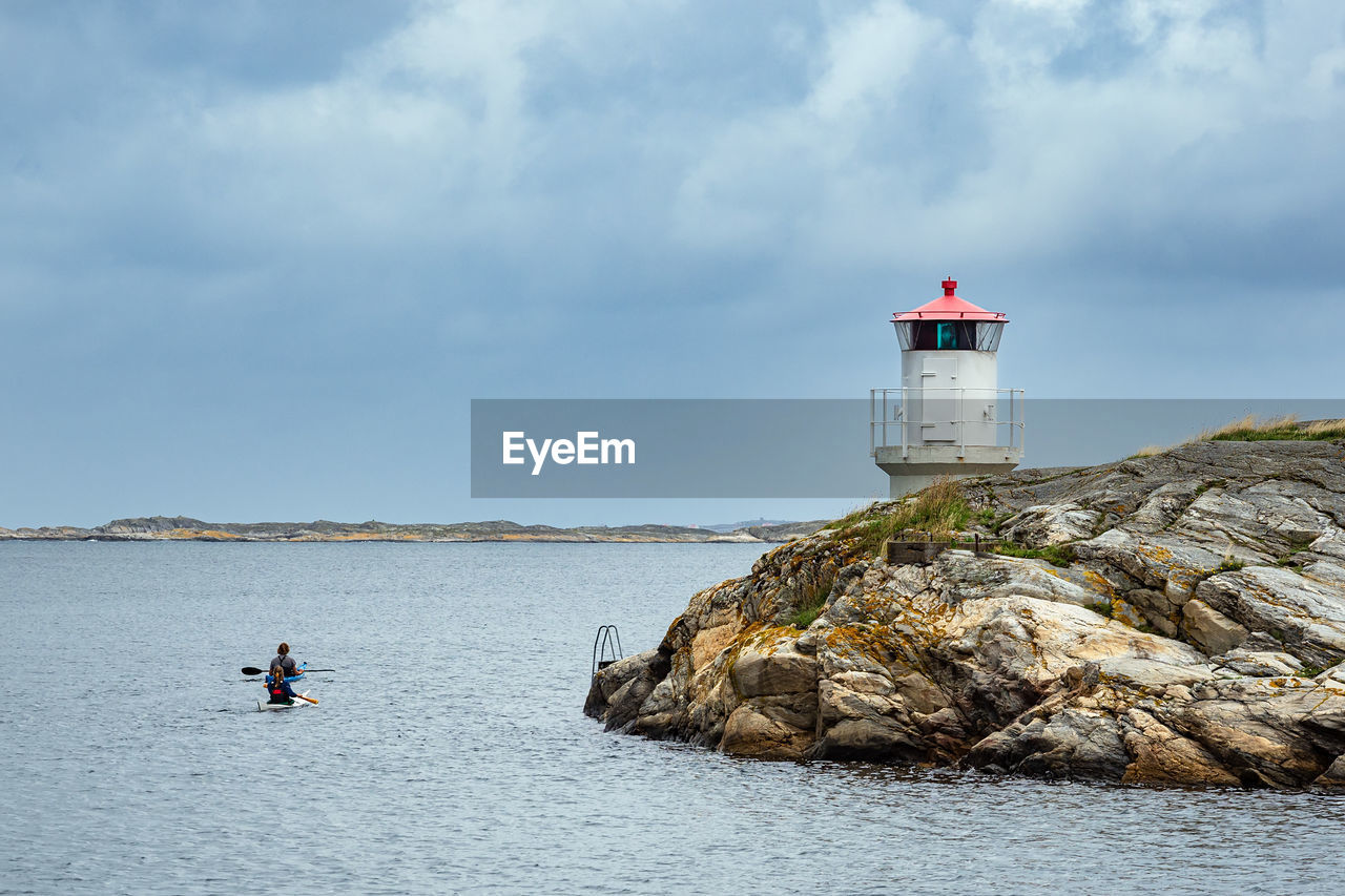 LIGHTHOUSE AMIDST ROCKS BY SEA AGAINST SKY