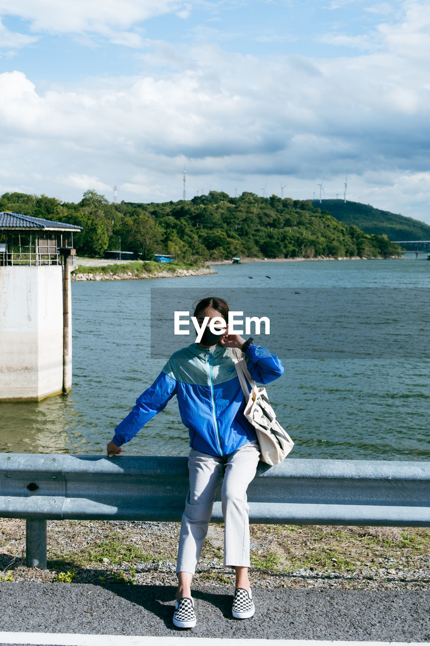 WOMAN STANDING BY LAKE AGAINST SKY