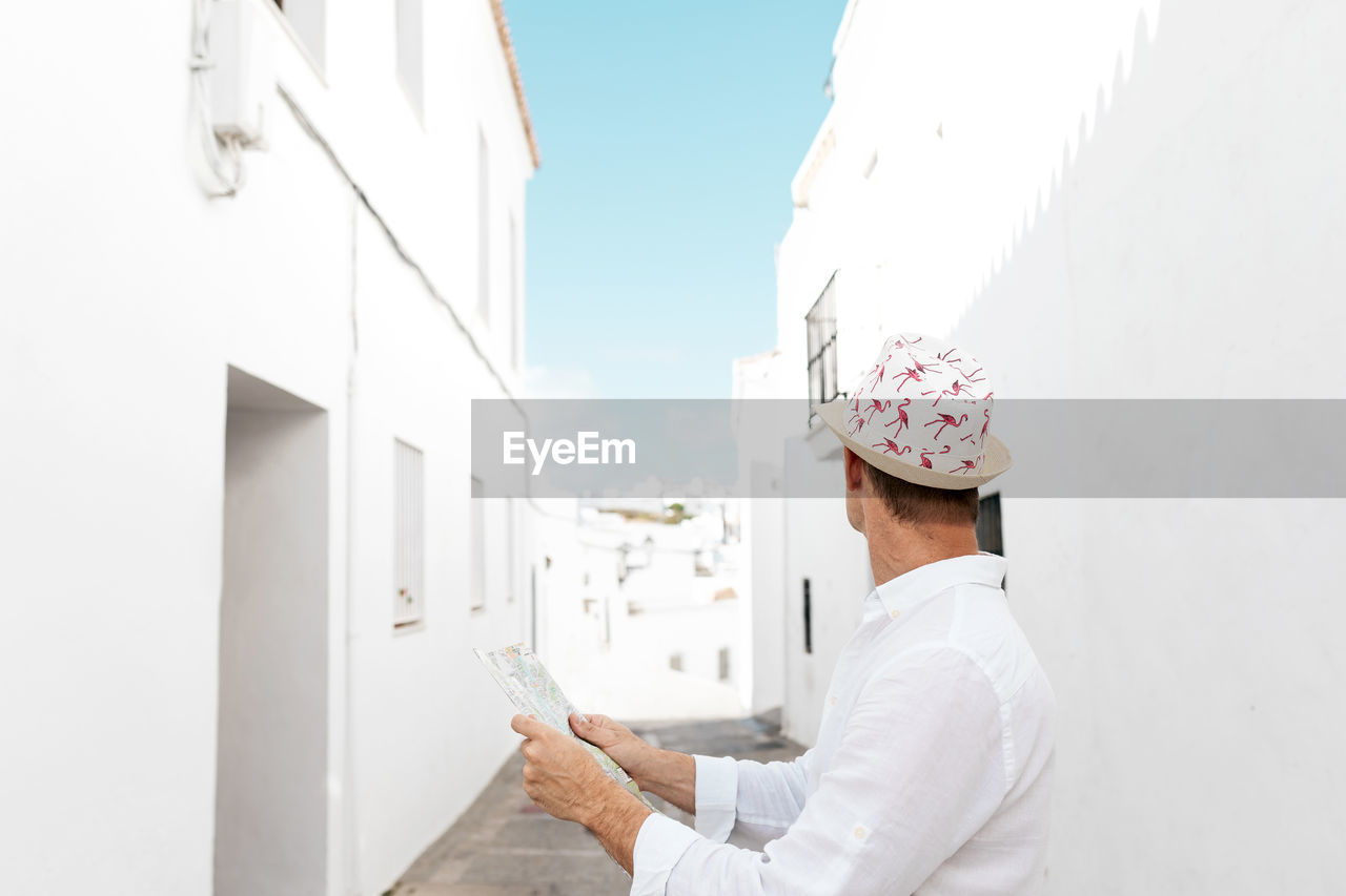 Side view of glad male traveler orienting himself with map on aged street in greece