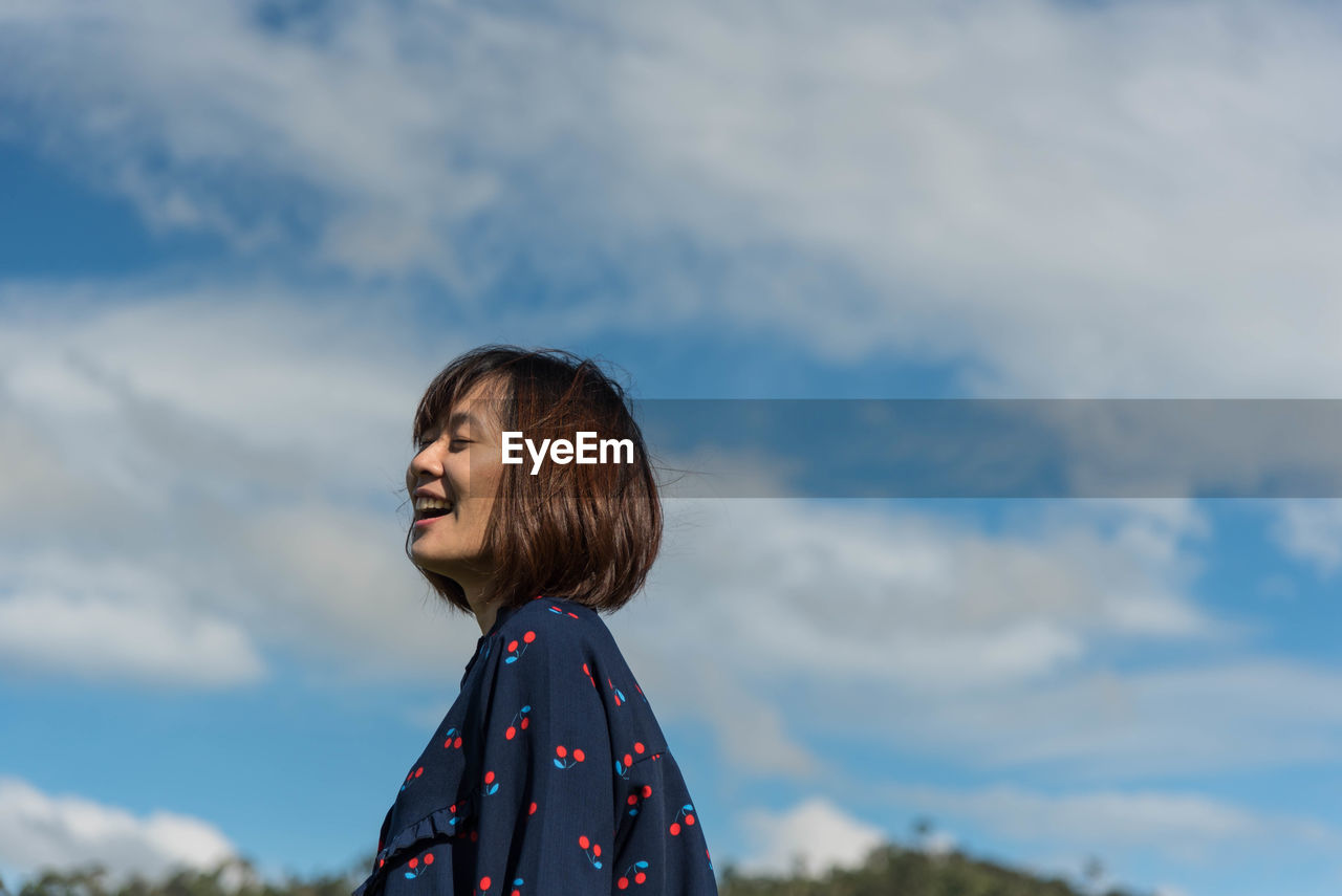 Low angle view of smiling beautiful woman against sky