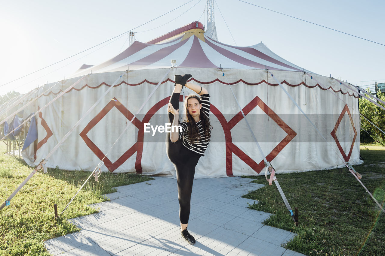 Female acrobat stretching while standing on one leg outside circus