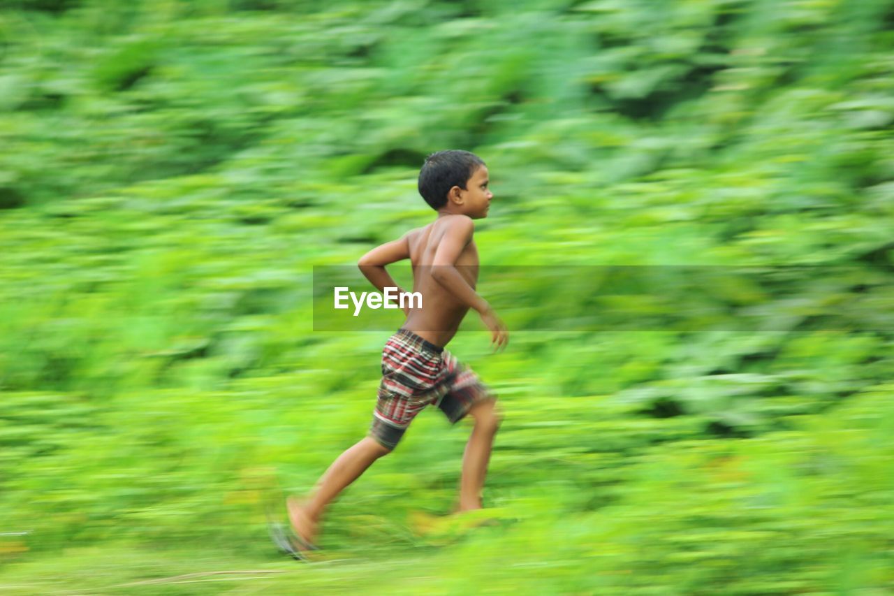 Blurred motion of shirtless boy running on field