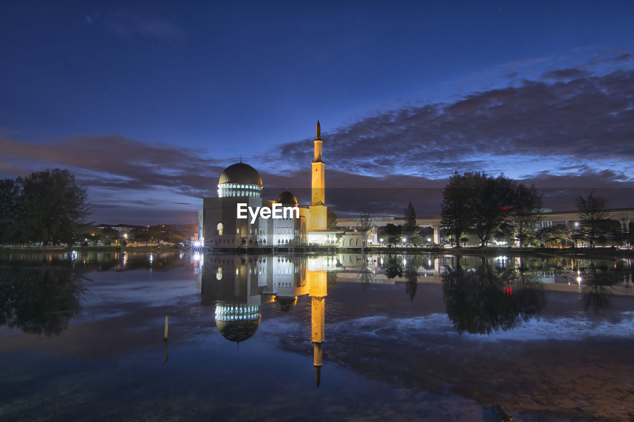 ILLUMINATED BUILDING BY LAKE AGAINST SKY AT DUSK