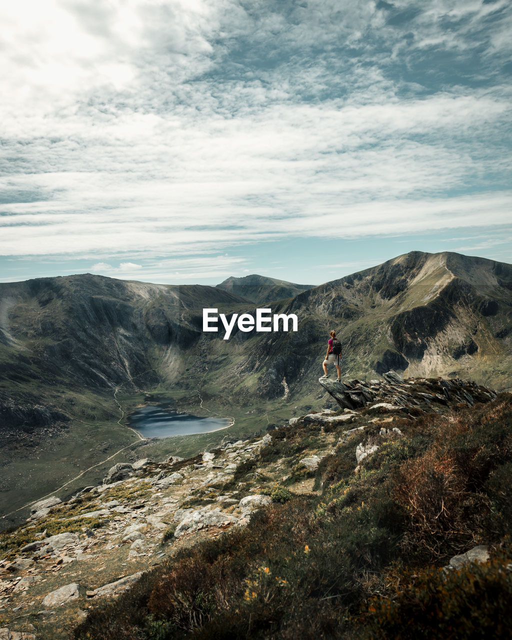 Scenic view of landscape against sky with a woman standing on a rock