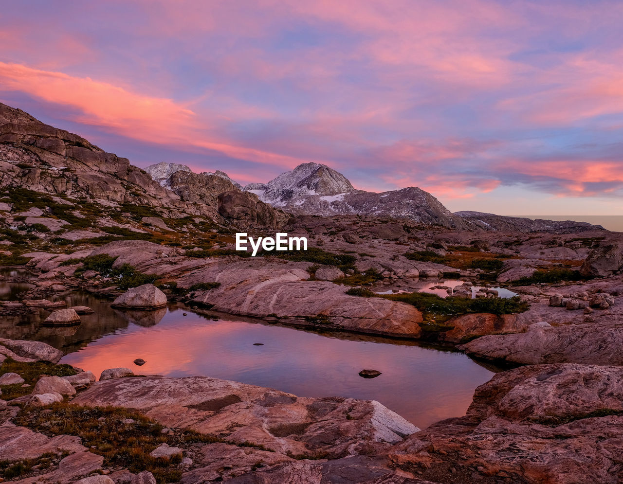 Scenic view of lake by mountains against sky during sunset