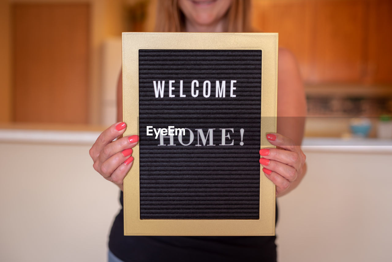 Midsection of woman holding sign at home