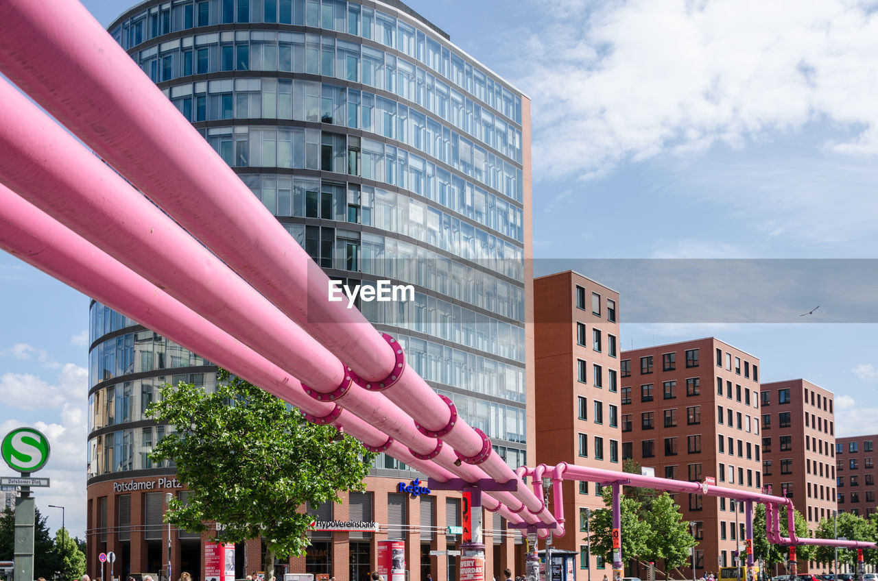 Pink pipes by modern buildings against sky