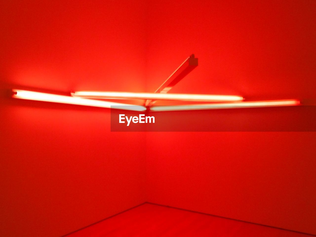 Low angle view of illuminated fluorescent lights on red wall