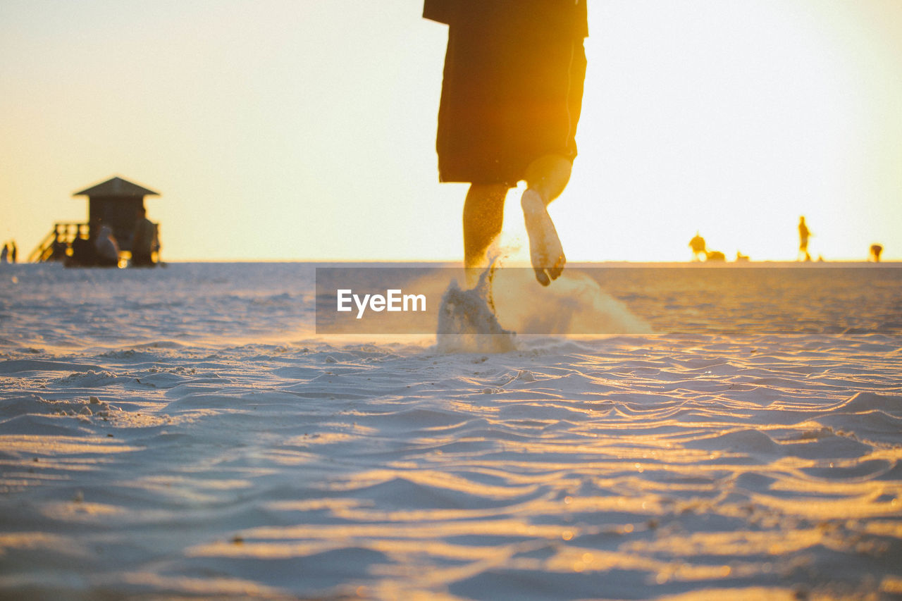 Low section of person on beach against sky during sunset