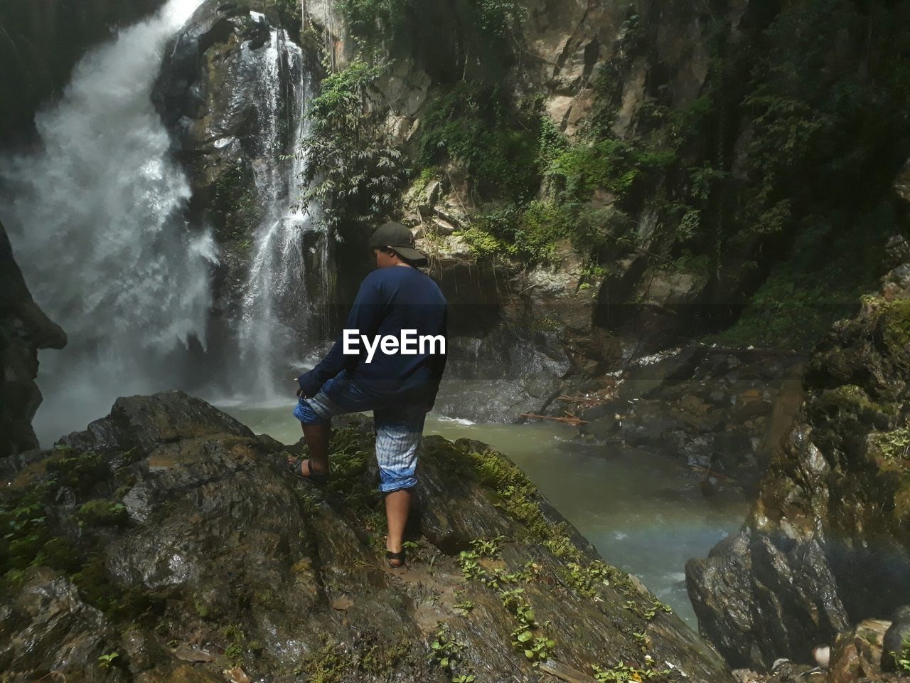 Rear view of woman standing on rock against waterfall