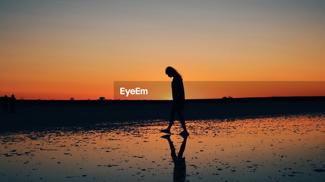 Silhouette woman walking at beach against sky during sunset