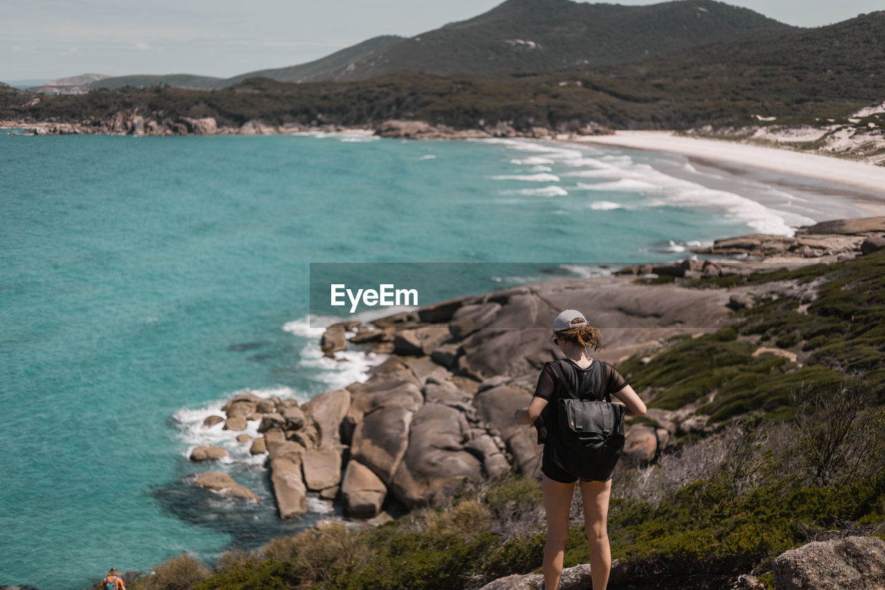 Rear view of woman standing on rock against sea