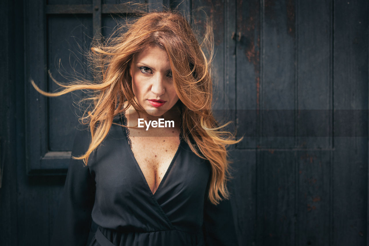 Portrait of mature woman with tousled hair standing against wall