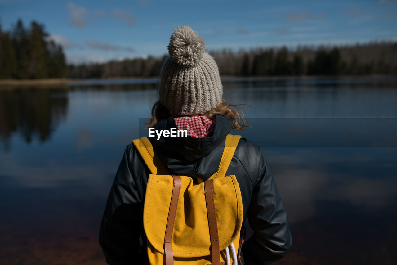 Rear view of person standing by lake against sky