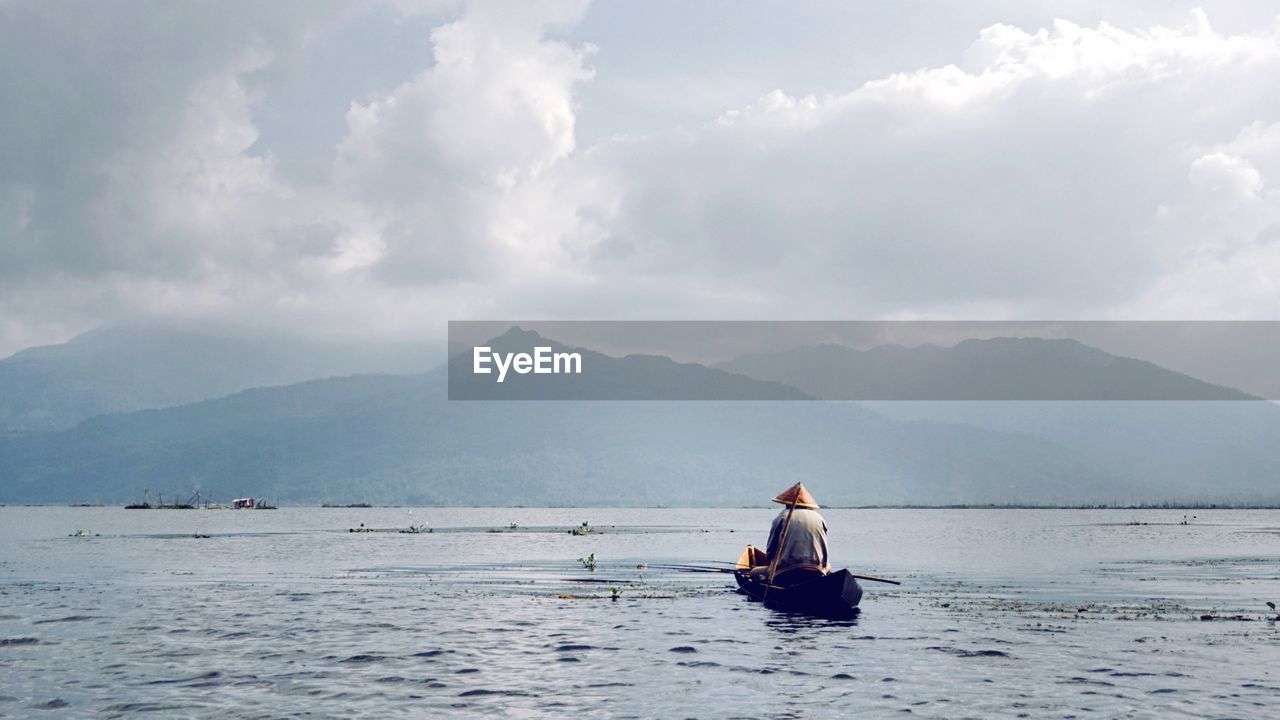 Fisherman sailing on boat in river against sky