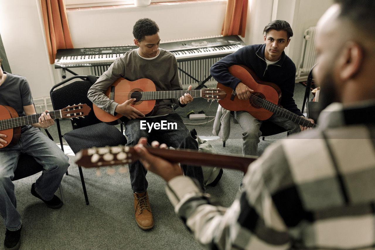 Male teenage students leaning guitar in music class at high school