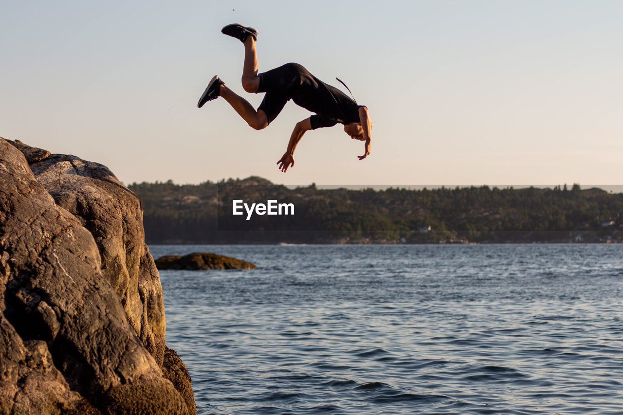 MAN JUMPING ON ROCK IN SEA