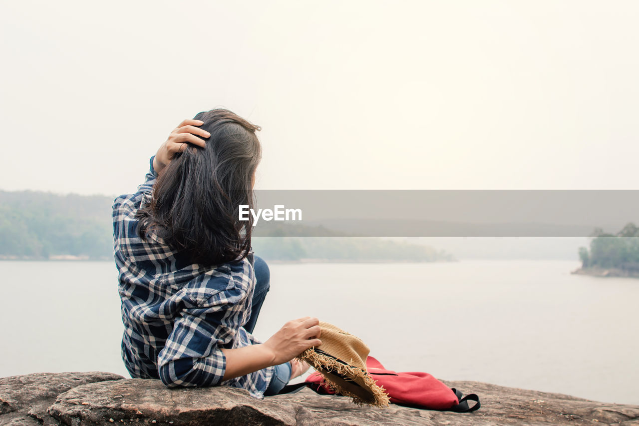 Young woman lying on rock by lake against clear sky