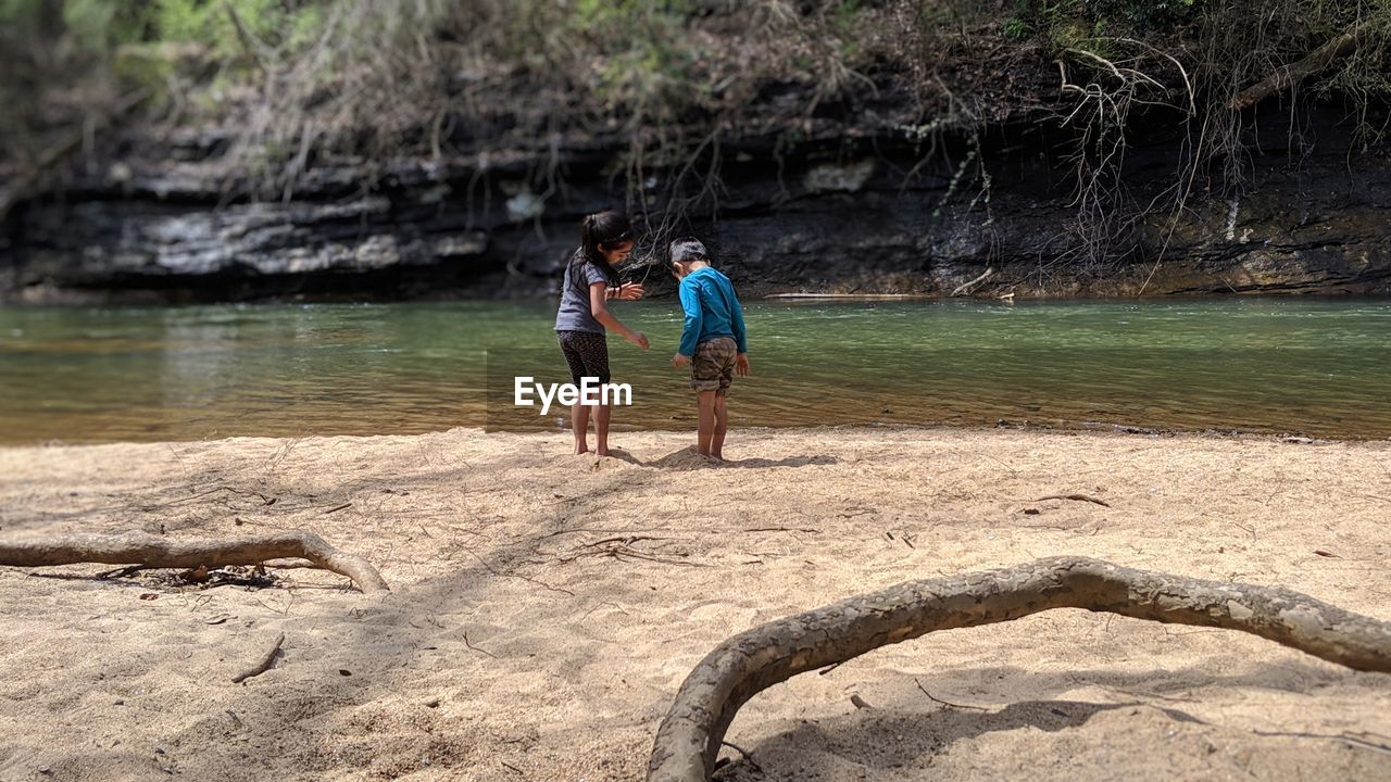 Rear view of siblings standing on sand by river