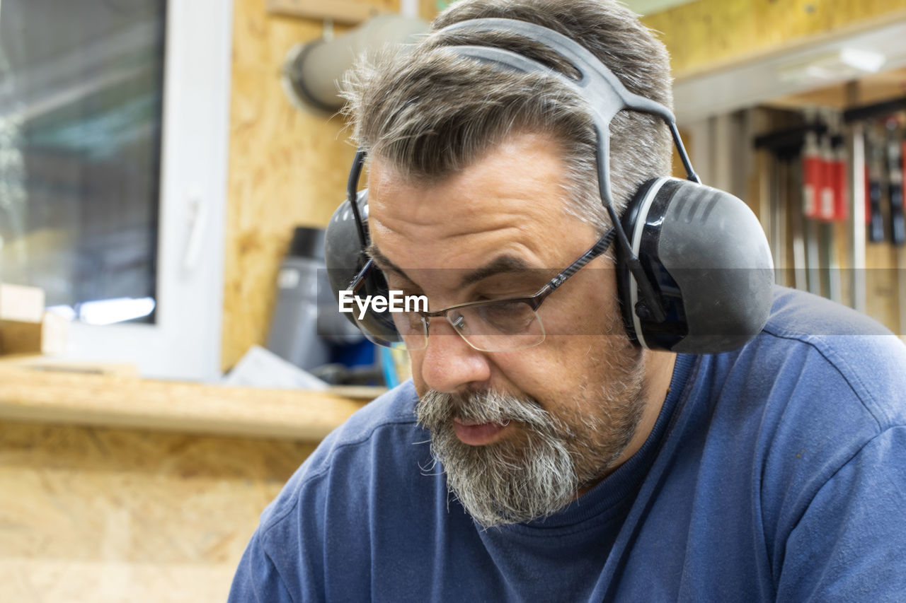 Manual worker wearing eyeglasses and ear protectors working in workshop