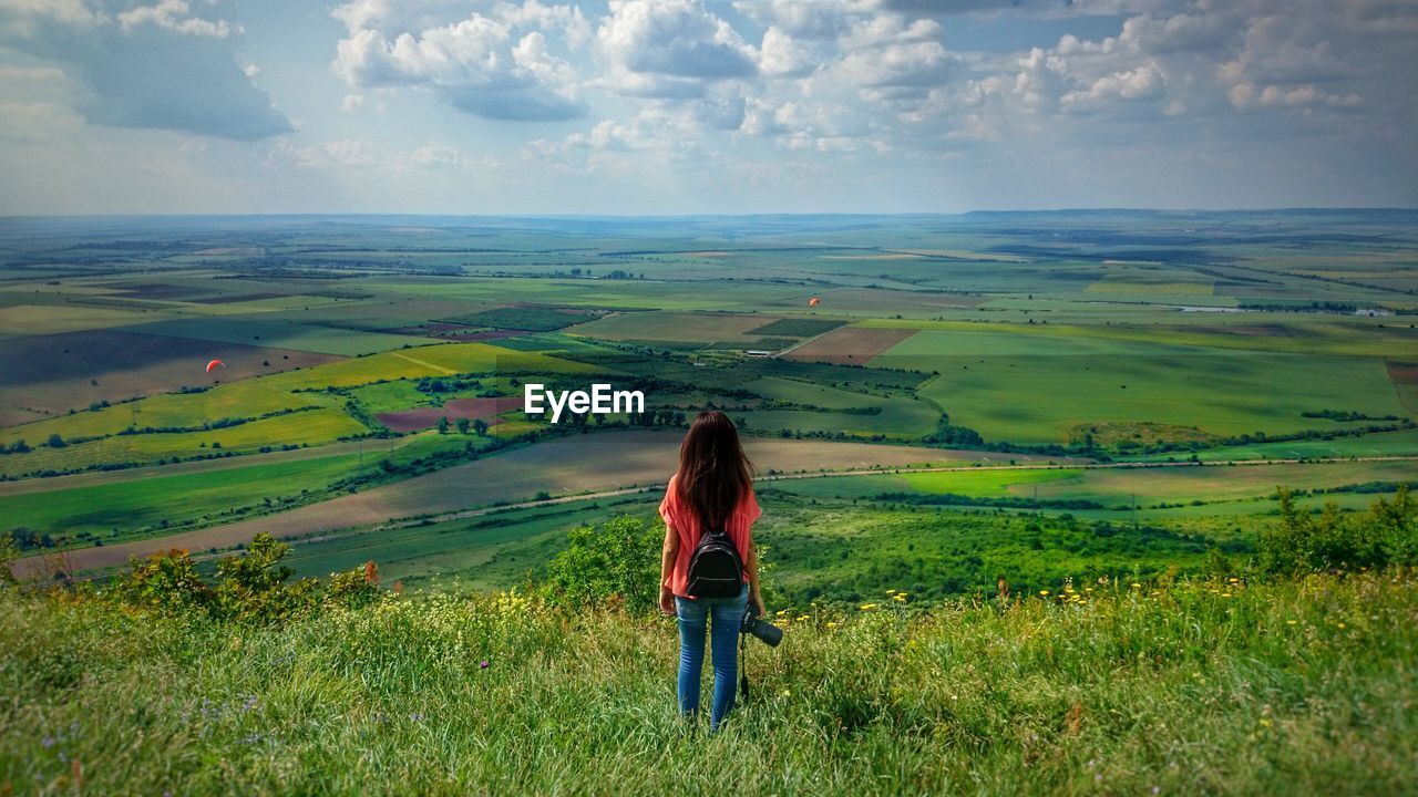 Rear view of female photographer standing on hill looking at green landscape