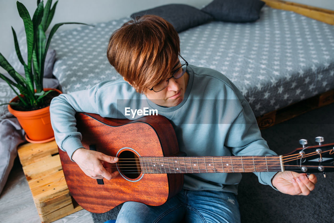 Woman with short hair enjoys playing guitar at home. music lessons for adults