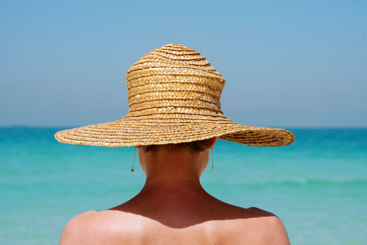 View from behind woman at the beach wearing straw hat against the sea