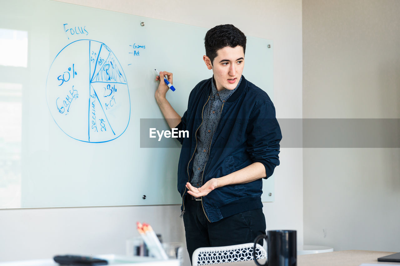 Confident young businessman discussing over diagram in board room at office