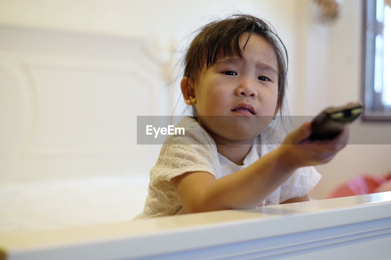 Portrait of girl watching tv while sitting on bed at home