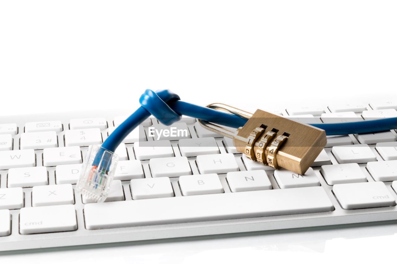 Close-up of padlock and cable on computer keyboard against white background