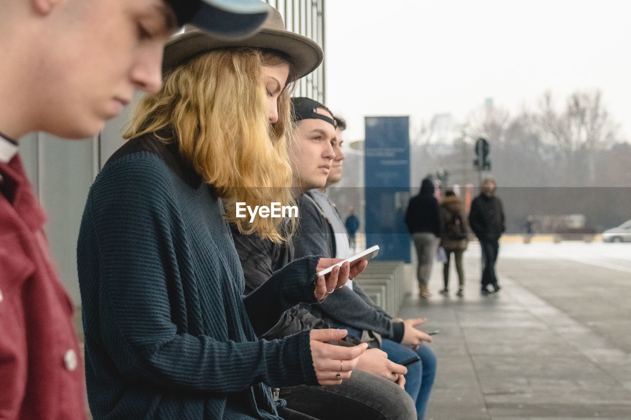 Side view of people sitting on footpath in city