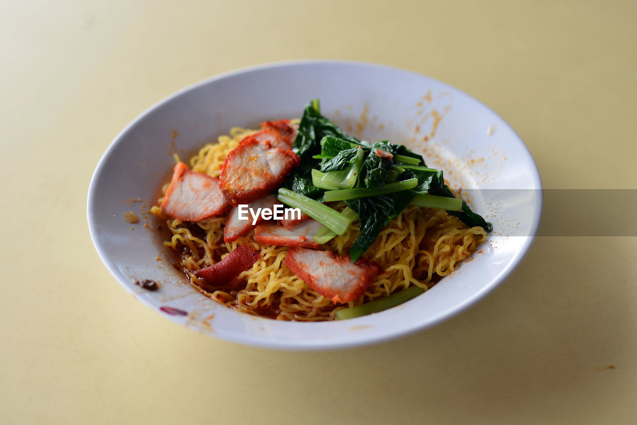 High angle view of wonton noodles with meat in white bowl on table